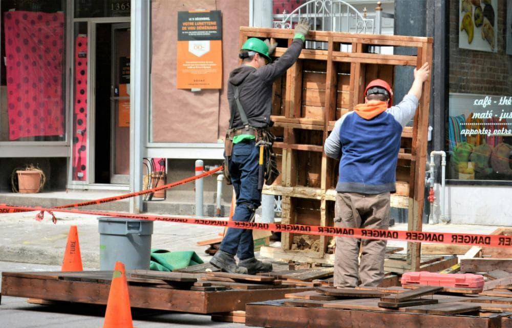Two construction workers raising a wooden frame on a Montreal street
