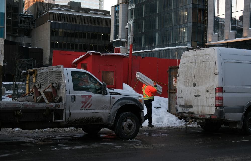 A worker in a high-visibility jacket carrying materials past a truck in downtown Montreal in winter