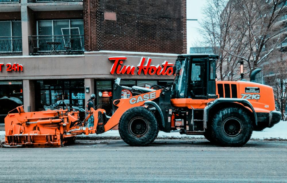 A snowplough clearing the street outside a Tim Hortons on a snowy Montreal morning